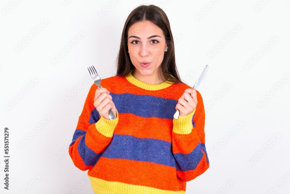 hungry Young caucasian woman wearing colorful knitted sweater over white background holding in hand fork knife want tasty yummy pizza pie hungry Young caucasian woman wearing colorful knitted sweater over white background holding in hand fork knife want tasty yummy pizza pie