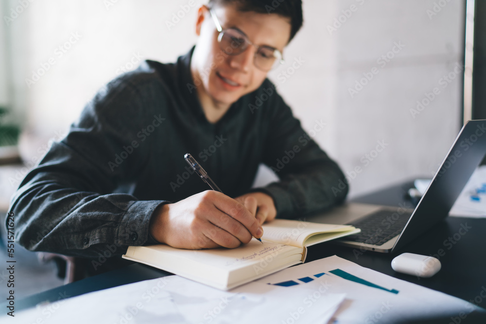 Cheerful man writing in notepad while working on laptop at home Cheerful man writing in notepad while working on laptop at home