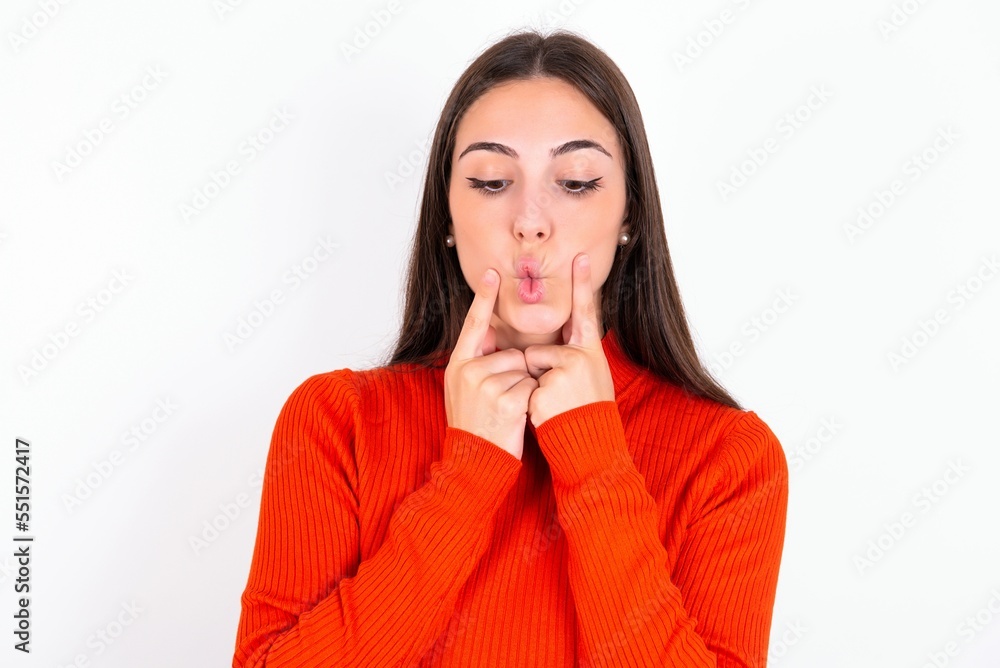 Young caucasian woman wearing red sweater over white background crosses eyes and makes fish lips funny grimace Young caucasian woman wearing red sweater over white background crosses eyes and makes fish lips funny grimace