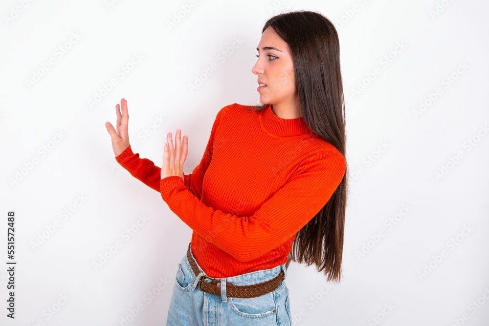 Displeased Young caucasian woman wearing red sweater over white background keeps hands towards empty space and asks not come closer sees something unpleasant Displeased Young caucasian woman wearing red sweater over white background keeps hands towards empty space and asks not come closer sees something unpleasant