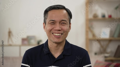 shoulder shot portrait of happy asian senior man looking at the camera with a big smile against modern cozy home background