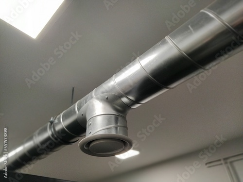 Extractor hood in a public toilet. Round metal pipe with gray air extractor. Engineering ventilation systems. Galvanized pipes under the ceiling of the room. Plastic round tip.