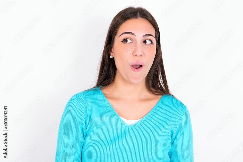 Shocked Young caucasian woman wearing blue sweater over white background look empty space with open mouth screaming: Oh My God! I can't believe this. Shocked Young caucasian woman wearing blue sweater over white background look empty space with open mouth screaming: Oh My God! I can't believe this.