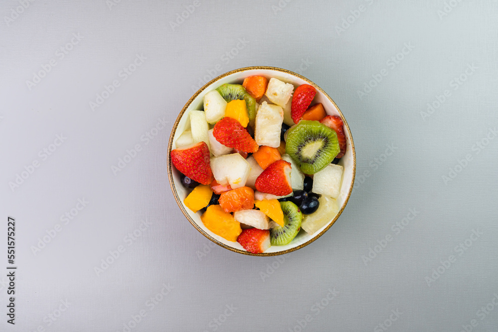 Fresh fruit salad in a bowl. Multicolored and tropical fruits. Pineapple, mango, grape, strawberry, papaya, melon, kiwi. Top view. Selective focus Fresh fruit salad in a bowl. Multicolored and tropical fruits. Pineapple, mango, grape, strawberry, papaya, melon, kiwi. Top view. Selective focus
