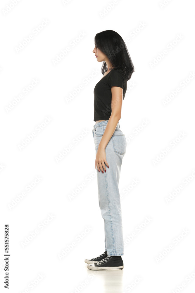 Fototapeta premium Side view of a young woman in loose jeans posing on white background