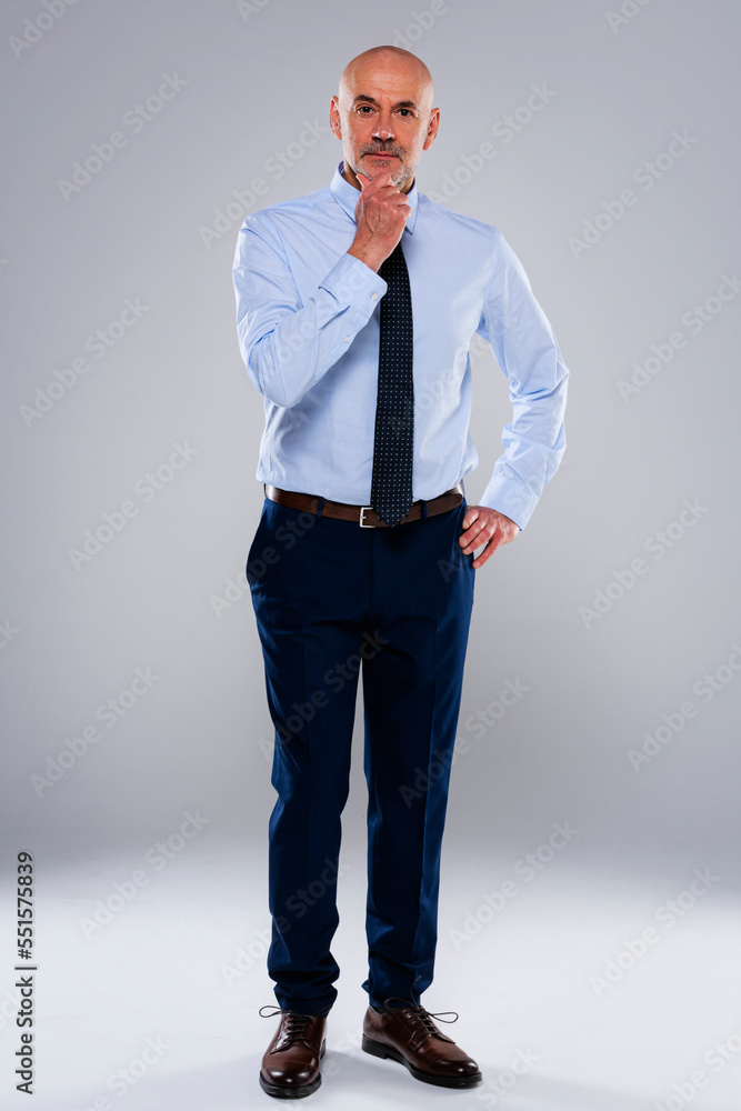 Serious faced mature male CEO standing at isolated grey background Serious faced mature male CEO standing at isolated grey background