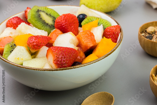 Fresh fruit salad in a bowl. Multicolored and tropical fruits. Pineapple  mango  grape  strawberry  papaya  melon  kiwi. Additional with chestnuts and granola. Selective focus