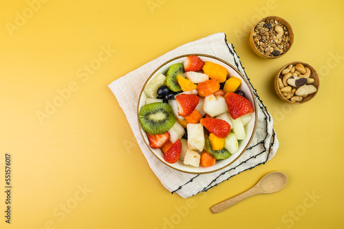 Fresh fruit salad in a bowl. Multicolored and tropical fruits. Pineapple, mango, grape, strawberry, papaya, melon, kiwi. Additional with chestnuts and granola. Top view. Selective focus