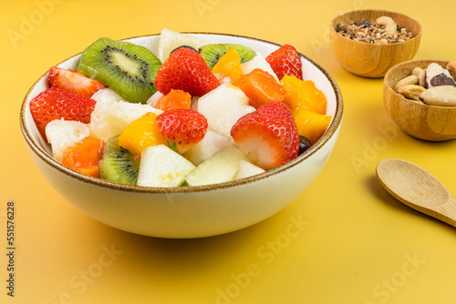 Fresh fruit salad in a bowl. Multicolored and tropical fruits. Pineapple  mango  grape  strawberry  papaya  melon  kiwi. Additional with chestnuts and granola. Selective focus