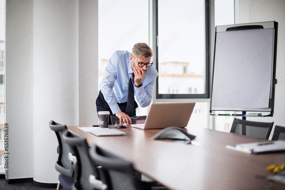 Stressed businessman standing at desk and having video conference meeting while working on laptop at the office Stressed businessman standing at desk and having video conference meeting while working on laptop at the office