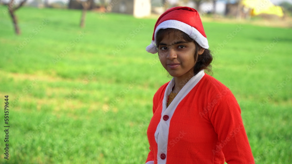 christmas, x-mas, winter, holidays and childhood concept - standing smiling little girl or preteen girl in santa helper hat and red dress over green field background. christmas, x-mas, winter, holidays and childhood concept - standing smiling little girl or preteen girl in santa helper hat and red dress over green field background.