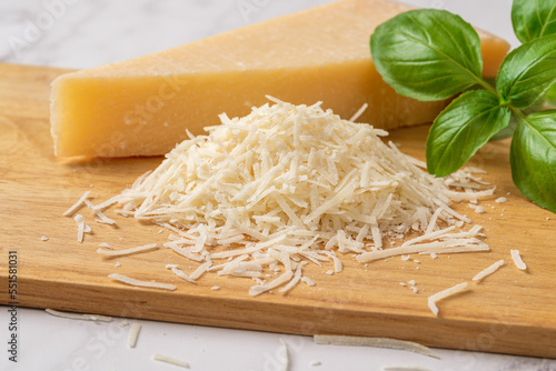 Shredded grana padano cheese on a cutting board. Italian parmesan cheese whole wedge and grated with green basil herb over wooden background. Delicious hard cheese. Dairy product. photo