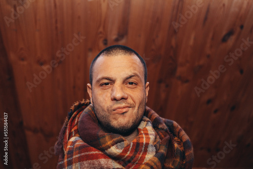 a man in a plaid on a wooden background with a satisfied expression