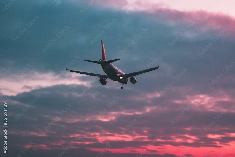 Passenger or cargo plane flies against the background of a red sky at sunset