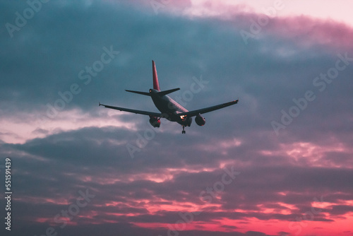 Passenger or cargo plane flies against the background of a red sky at sunset
