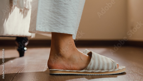 Close-up Asian girl foot step down on bed with white pajamas wear slipper walk to open curtain on window fresh peaceful morning light empty floor in bedroom at home. Female morning lifestyle concept.