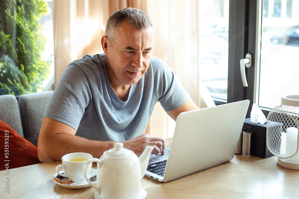 Busy concentrated passionate grizzled mature businessman working on laptop in cafe, drink tea in cafe. Online technology Busy concentrated passionate grizzled mature businessman working on laptop in cafe, drink tea in cafe. Online technology