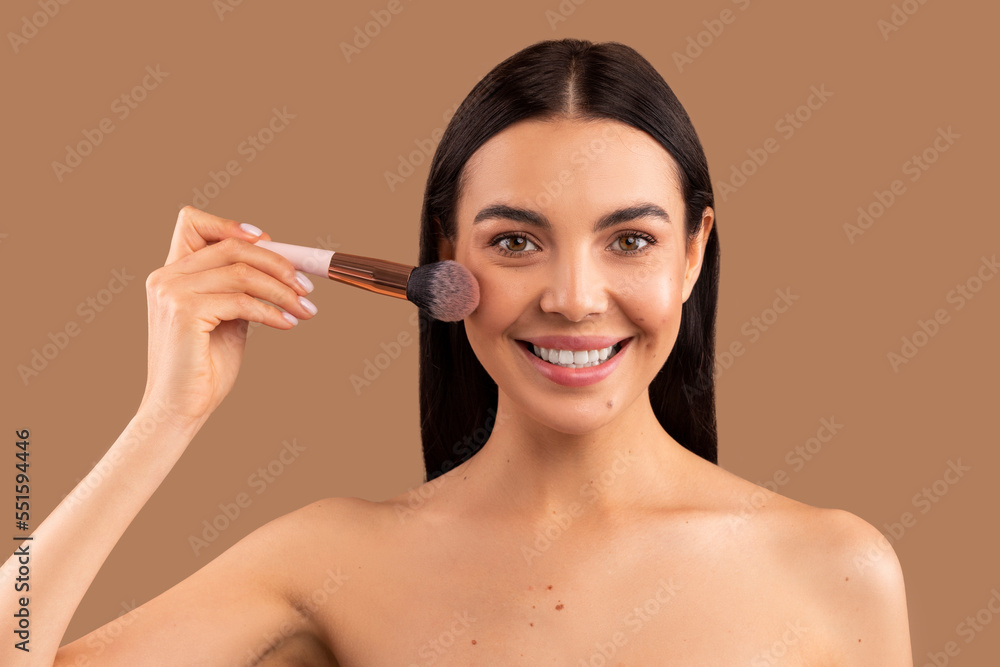 Headshot of youngsmiling beautiful woman holding makeup brush, applying blush Headshot of youngsmiling beautiful woman holding makeup brush, applying blush