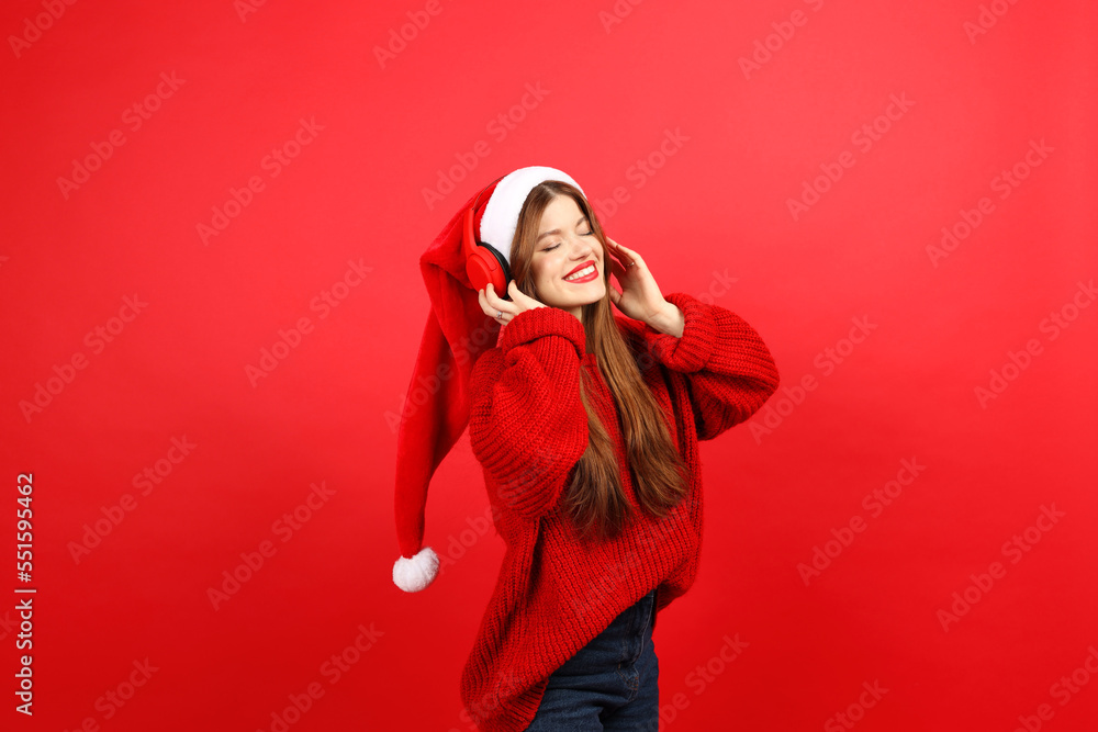 Dance music for christmas, playlist for christmas celebration. Happy and carefree young woman in headphones and santa hat on red background. Dance music for christmas, playlist for christmas celebration. Happy and carefree young woman in headphones and santa hat on red background.