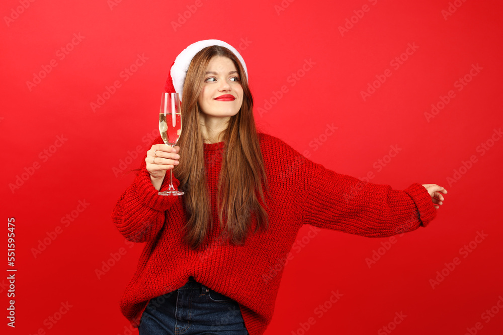 Happy girl in santa hat with a glass of champagne on a red background. Happy girl in santa hat with a glass of champagne on a red background.