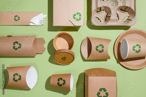 The concept of recycling and zero waste. Biodegradable paper tableware for food on a green background with a recycling sign. View from above.