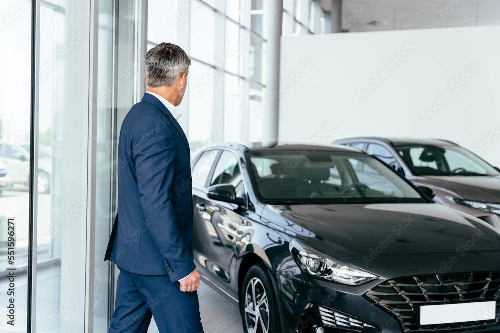 Side view confident happy businessman male client man 45s wear blue suit enter office looking aside in car showroom dealership salon store indoors. Business lifestyle sales concept. Side view confident happy businessman male client man 45s wear blue suit enter office looking aside in car showroom dealership salon store indoors. Business lifestyle sales concept.