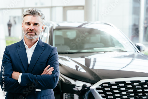 Wallpaper Mural Portrait of handsome aged man standing besides car in showroom posing next to new car, wearing formal suit Torontodigital.ca