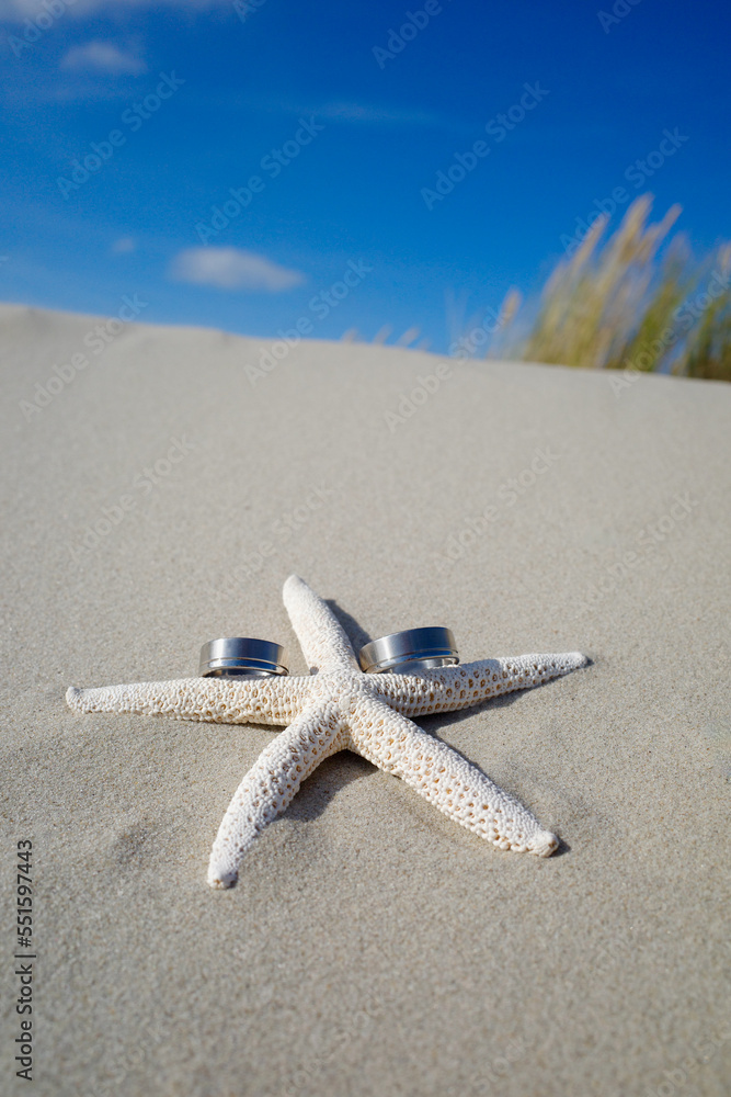 Vertical image of starfish with wedding rings on the beach. Summert wedding invitation or background.