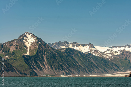 Resurrection Bay, Alaska, USA - July 22, 2011: West side of bay landscape where glacier reaches the bay water under blue sky. Plenty of snow patches on the dark rock mountain range photo