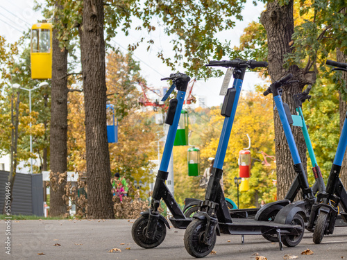 Electric Scooters standing on asphalt road in autumn park with colorful cableway cabins. Public e-scooter parking in Kharkiv city recreation park