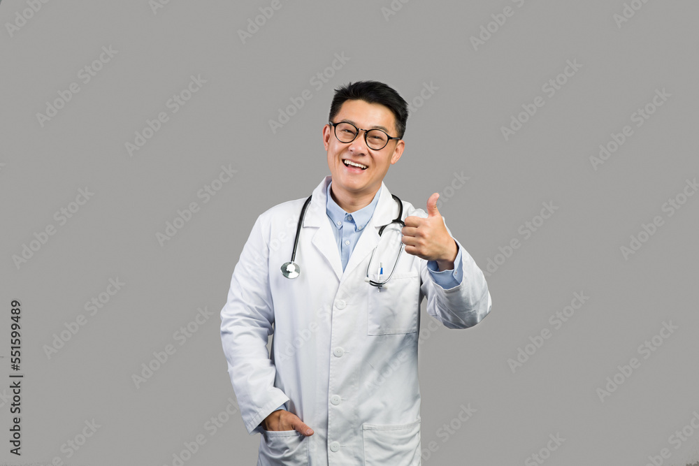 Cheerful middle aged japanese male therapist in white coat and glasses showing thumb up, advice medicine Cheerful middle aged japanese male therapist in white coat and glasses showing thumb up, advice medicine