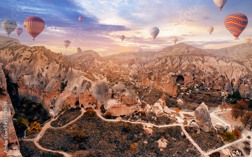 Cave house dwellings of Cappadocia, national park Goreme of Nevsehir Turkey with hot air balloons with sunlight, aerial drone view