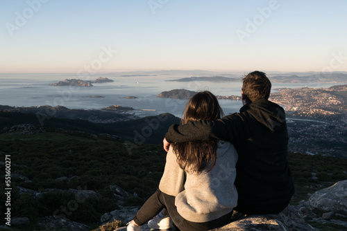 Rear view of a couple sitting on a mountain looking at view of Cies Islands, Baiona and Nigran, Val Minor, Pontevedra, Galicia, Spain photo