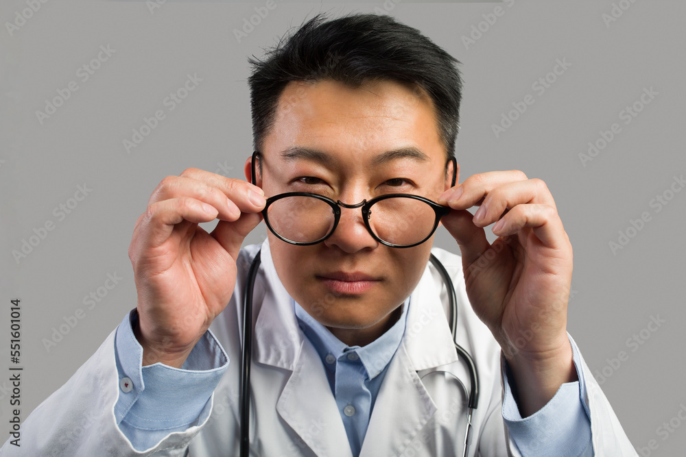 Serious suspects middle aged asian male therapist in white coat takes off glasses, looks at camera