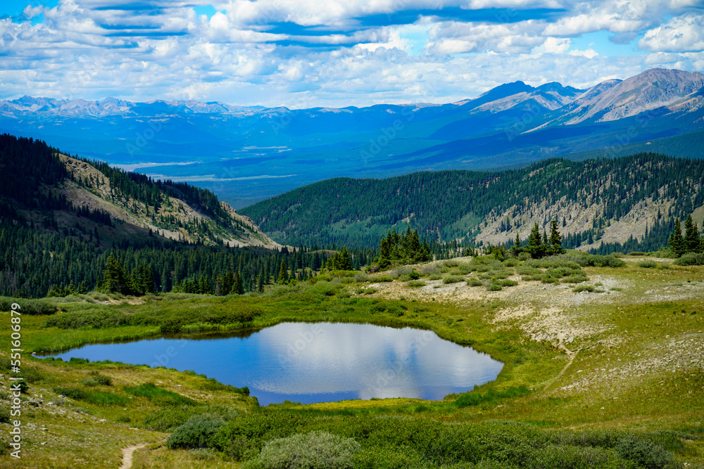 An alpine lake atop a Colorado mountain pass reflects the colors of a clouded blue sky.