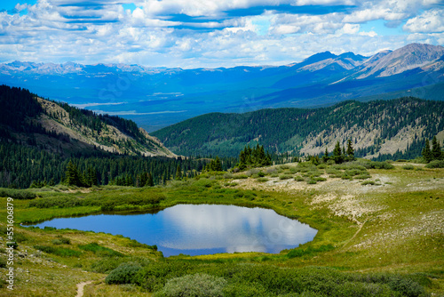 An alpine lake atop a Colorado mountain pass reflects the colors of a clouded blue sky.