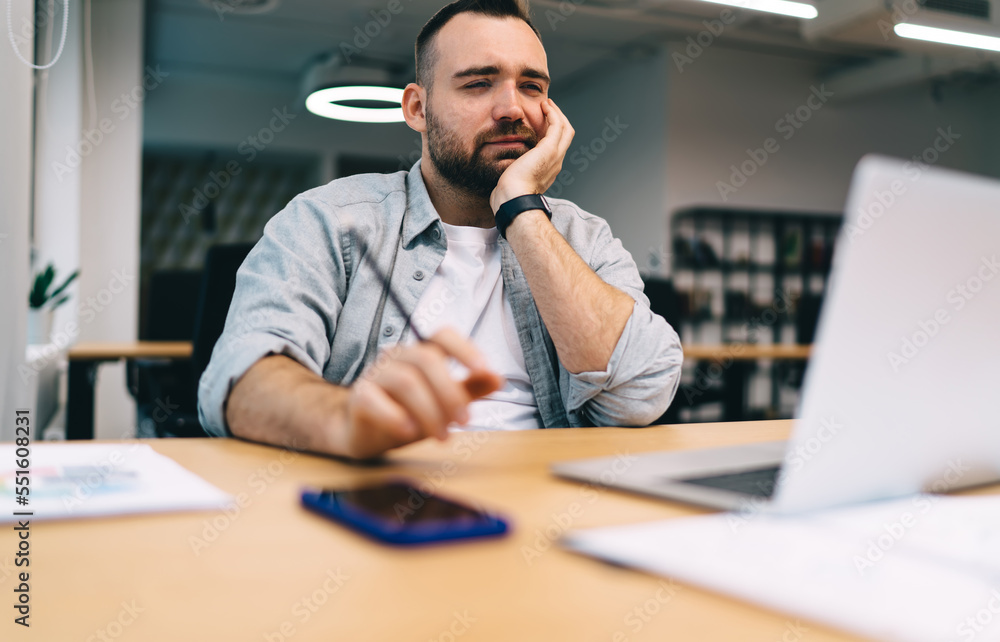 Thoughtful man sitting at table and working on project in office Thoughtful man sitting at table and working on project in office