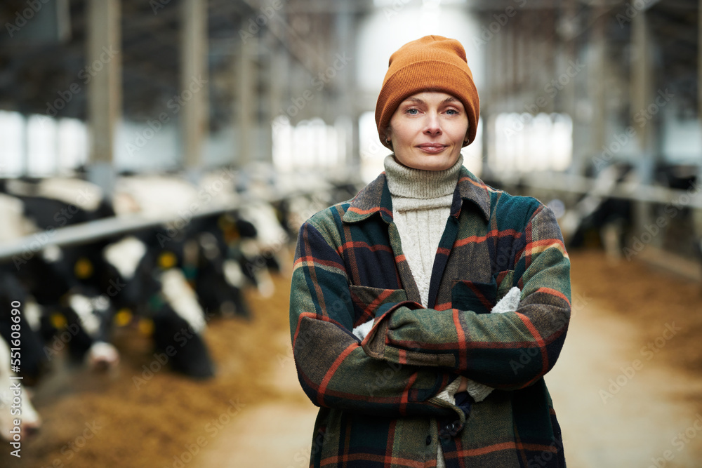 Young successful female owner of cowfarm in workwear standing in front of camera with her arms crossed on chest against cowsheds Young successful female owner of cowfarm in workwear standing in front of camera with her arms crossed on chest against cowsheds