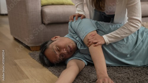 Closeup of unconscious Asian senior male grandfather lying on floor with hand of his family shaking his body and tapping his face trying to wake him up.