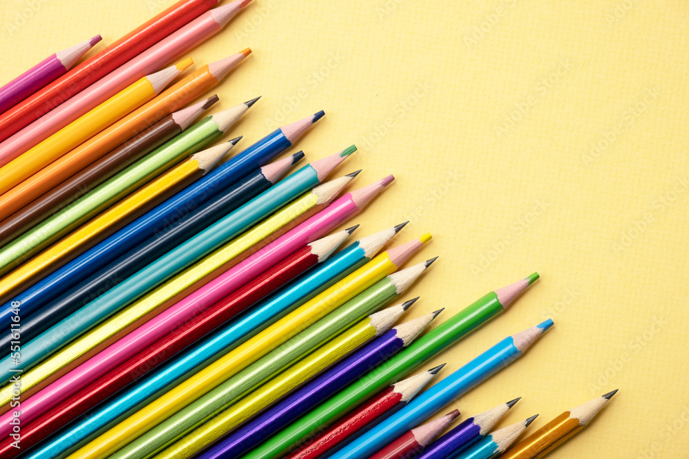 There are many different colored pencils scattered on a colored background.