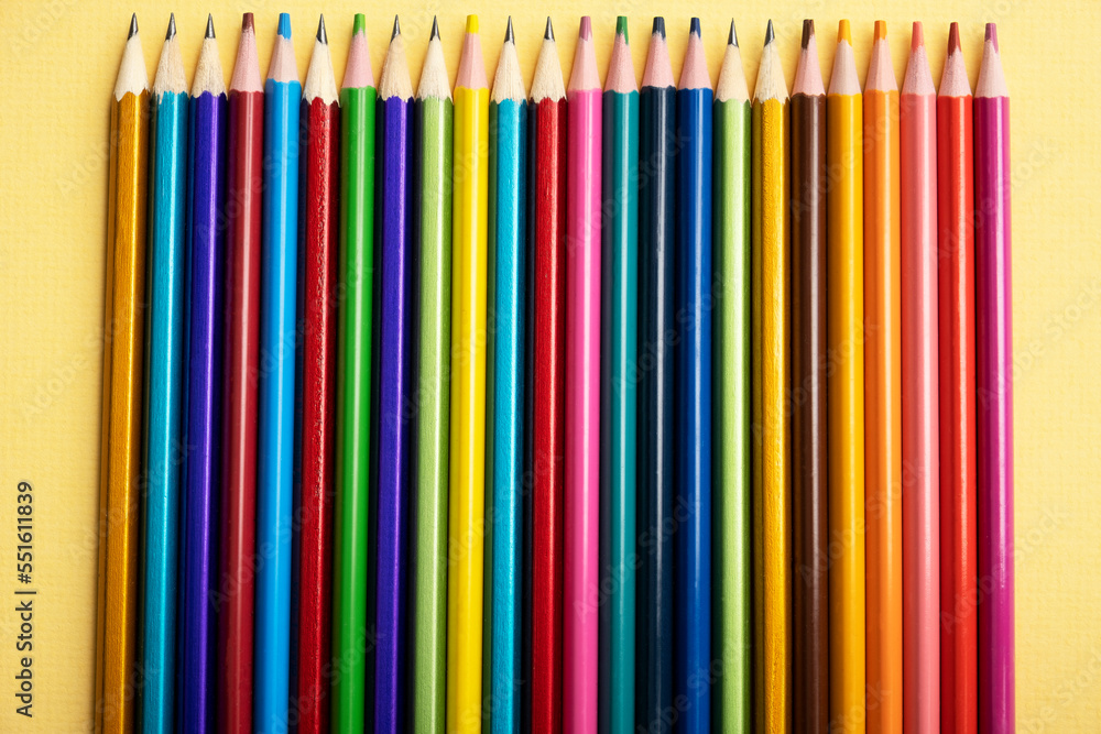 There are many different colored pencils lying exactly in a row on a colored background. There are many different colored pencils lying exactly in a row on a colored background.