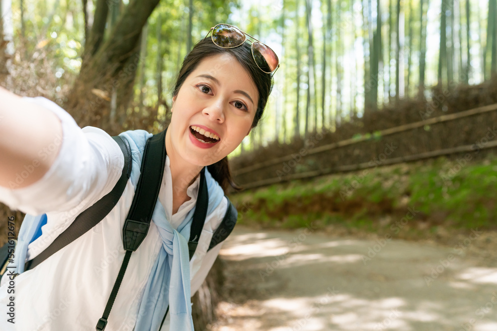 happy asian chinese girl tourist wearing sunglasses on head and taking self portrait in Arashiyama Bamboo Grove in Kyoto japan. she looks at mobile camera with big smile on face. happy asian chinese girl tourist wearing sunglasses on head and taking self portrait in Arashiyama Bamboo Grove in Kyoto japan. she looks at mobile camera with big smile on face.