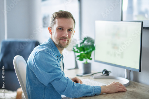 Young handsome IT support man in denim shirt . Attractive bearded caucasian male freelance software engineer sitting at working place in office hardly working using computer. High quality image