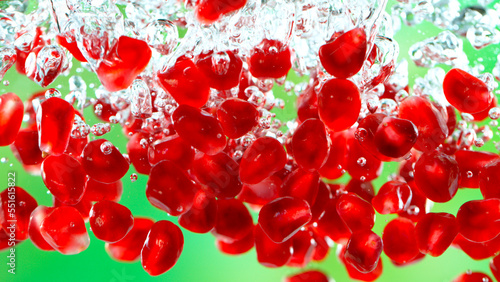 Fresh pomegranate pieces falling into water, green background