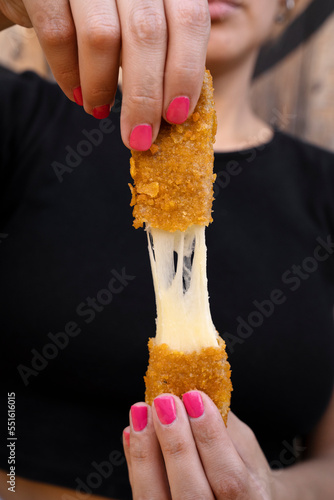Woman stretching fried mozzarella cheese sticks.	