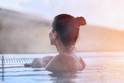 Woman enjoying view, relaxing in outdoor thermal pool on a winter day. Snowy mountains on the background.