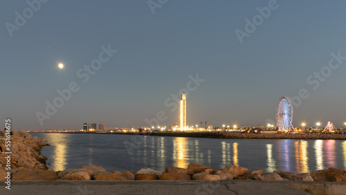 The great mosque and ferris wheel under moonlight seen from Sablette promenade jetty. Skyline view of Algiers city by night, water reflexion lights illuminated by colorful world biggest minaret.