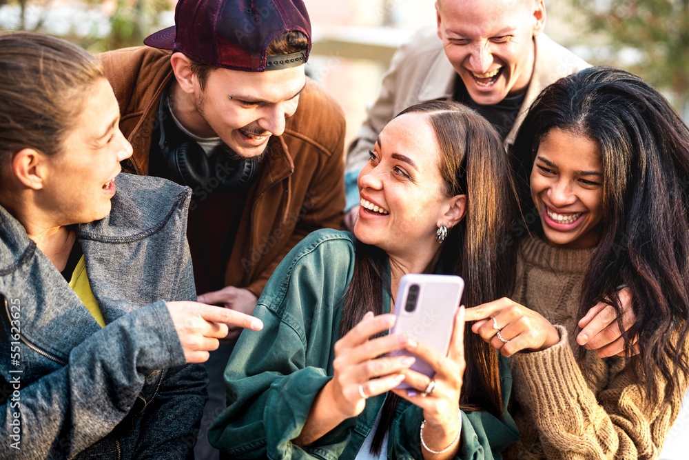 Fototapeta premium Multicultural young people having fun with mobile phone at urban city yard - Happy guys and girls spending time together sharing funny content online on smartphone social networks - Bright warm filter