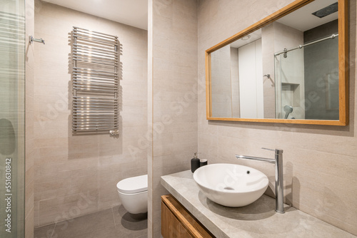 Interior of modern tiled bathroom with white toilet  radiator and shower in reflection of wooden framed mirror.