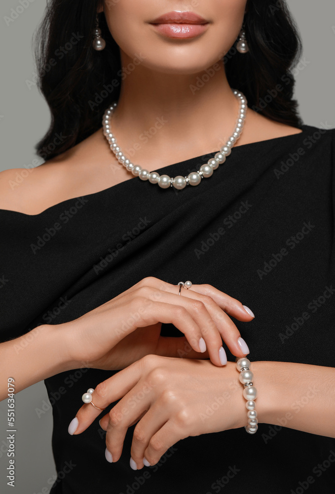 Young woman wearing elegant pearl jewelry on grey background, closeup